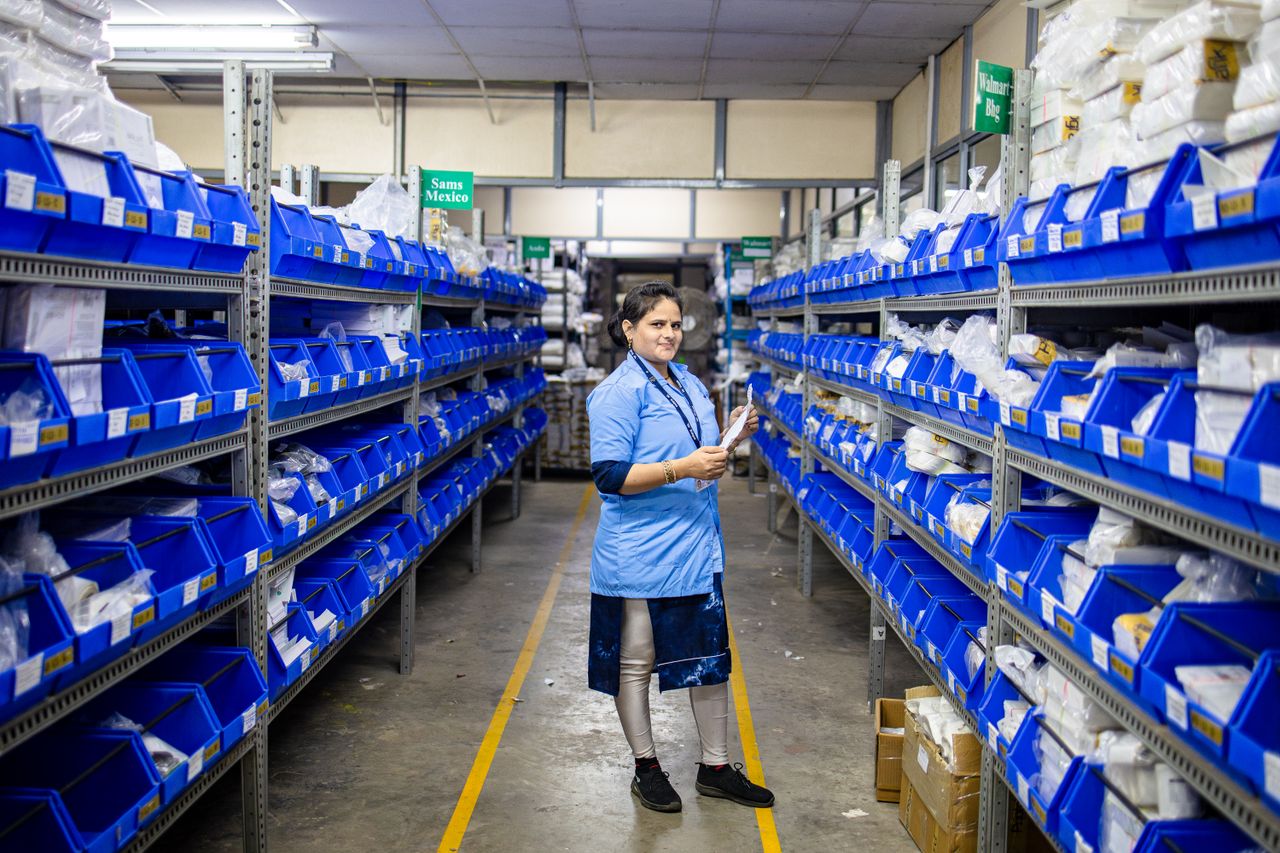 Female worker organizing inventory in a modern warehouse aisle, surrounded by blue storage bins.